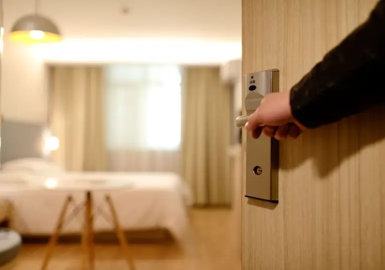 Room with a neat single bed, lit by a bedside lamp